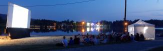 personnes devant un projecteur blanc, de nuit, assis face à à un lac ou la mer, qui attendent