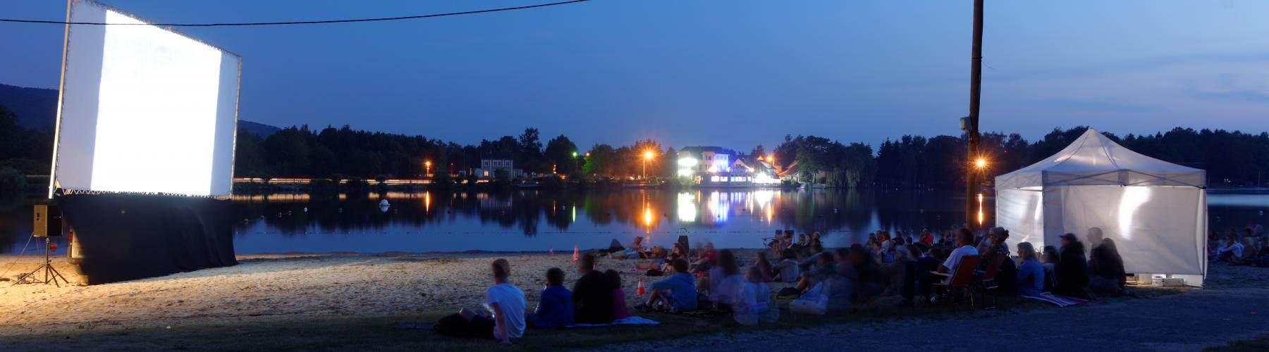 personnes devant un projecteur blanc, de nuit, assis face à à un lac ou la mer, qui attendent