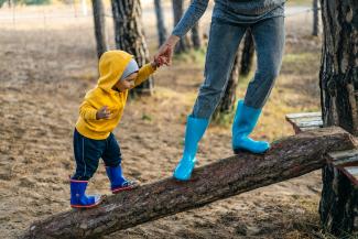 enfant qui marche sur un tronc d'arbre aidé par un adulte