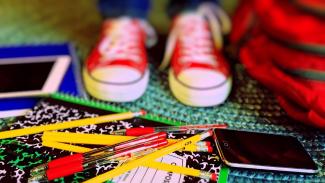 baskets d'enfant rouges devant sac, crayons, cahiers, tablette, smartphone au sol