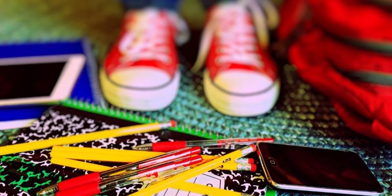 baskets d'enfant rouges devant sac, crayons, cahiers, tablette, smartphone au sol